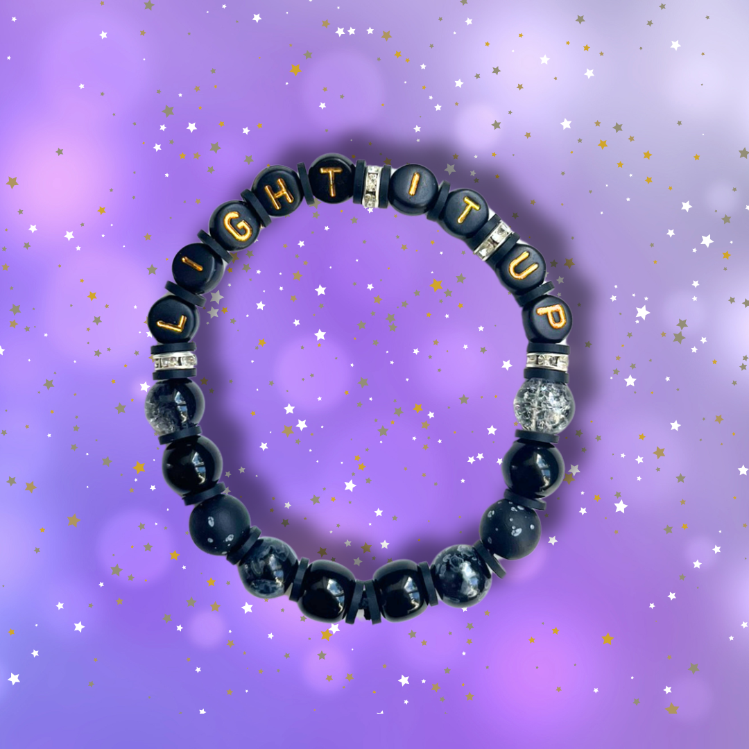 Black beaded bracelet with the words Light It Up, on a purple background with stars.