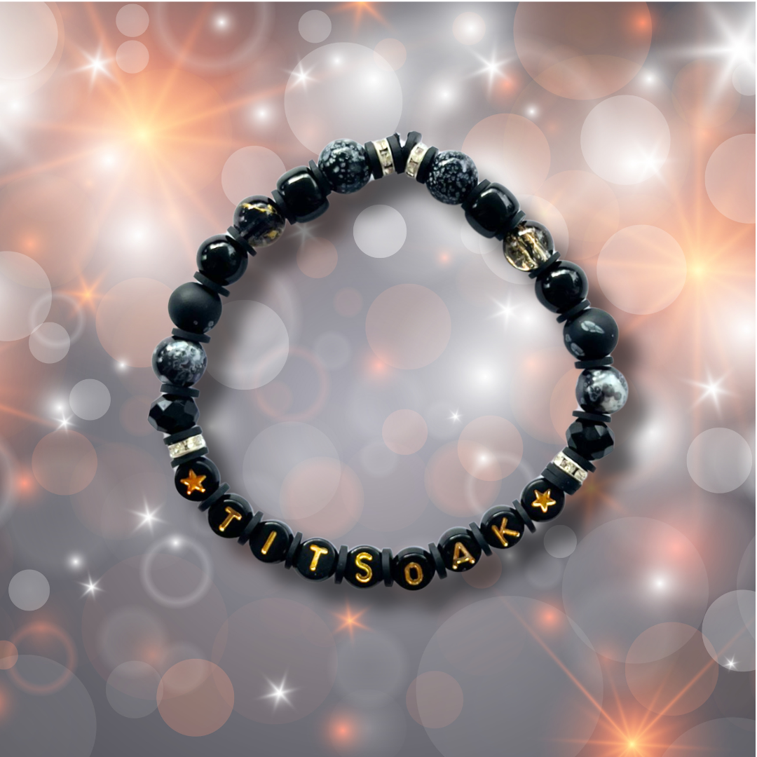 Black beaded bracelet with the letters TITSOAK, on a sparkly background.