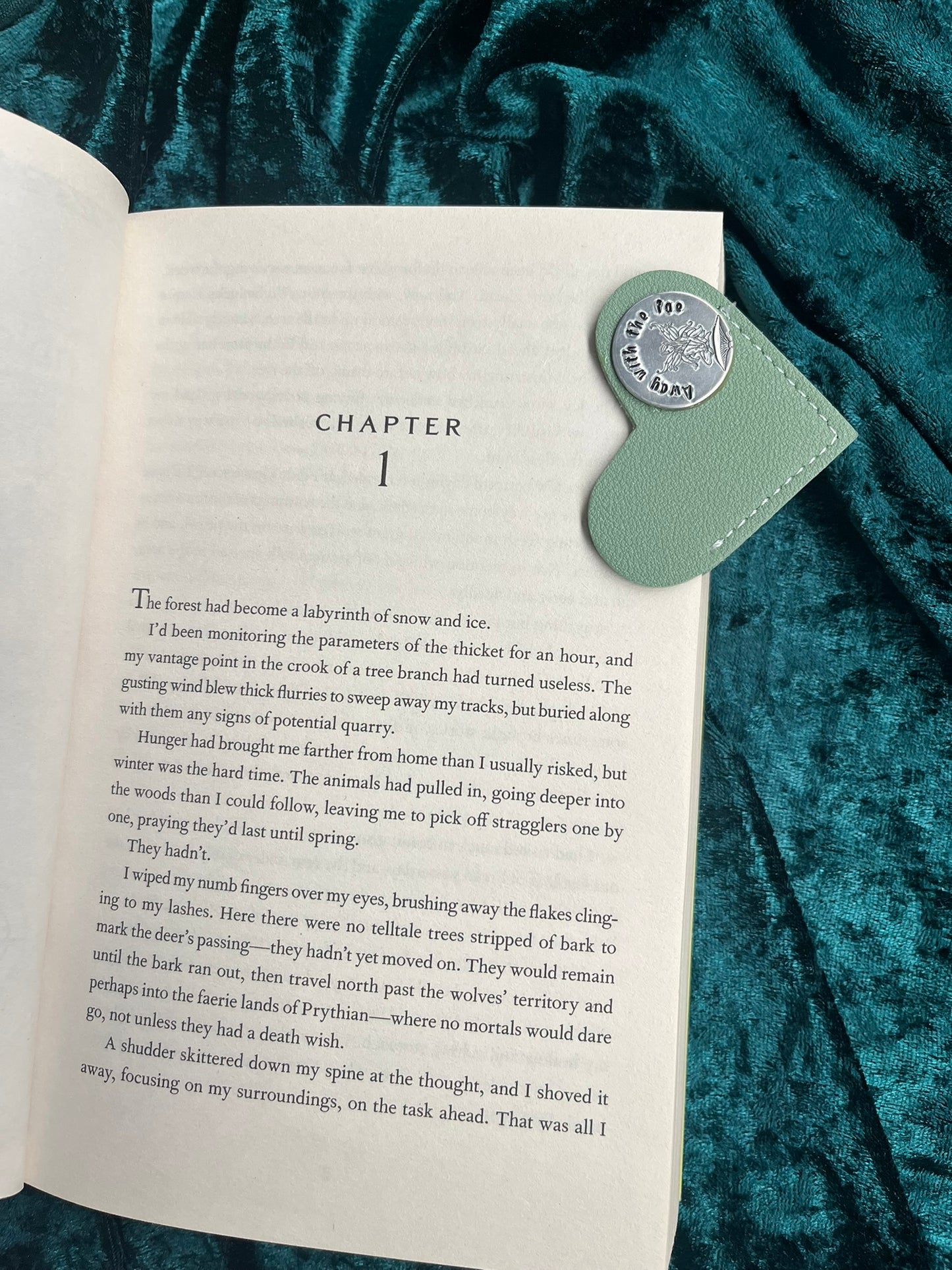 Open book with a heart-shaped green leather bookmark on a textured teal fabric background