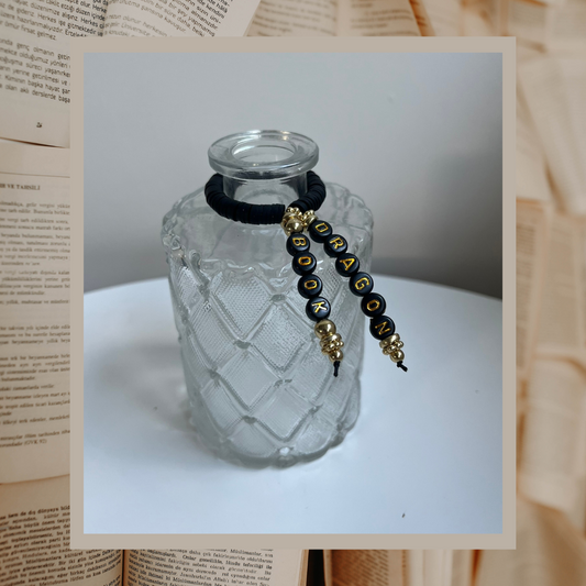 Glass vase with beads that say Book Dragon. Shown on an open books background.