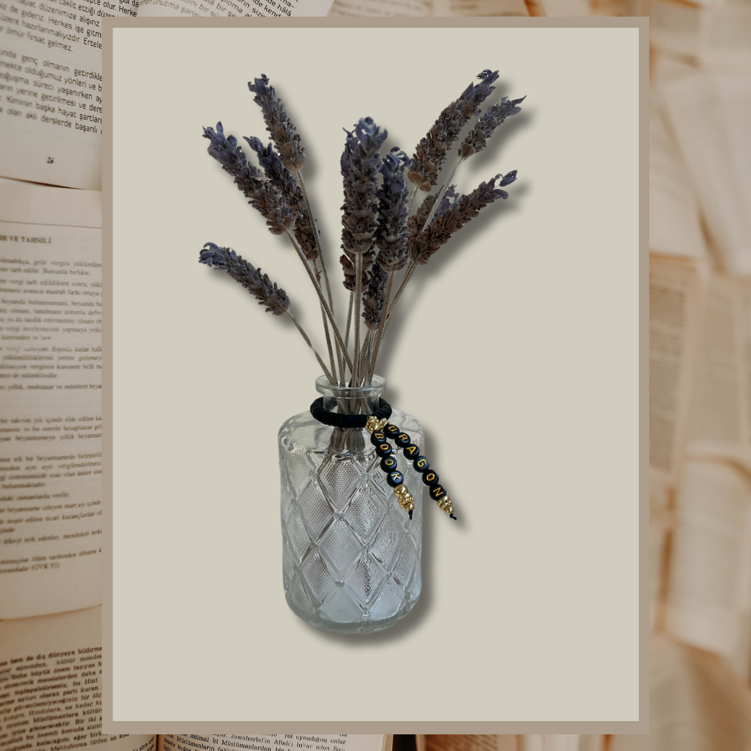 Glass vase with beads that say Book Dragon. Vase with lavender in it, shown on an open books background.