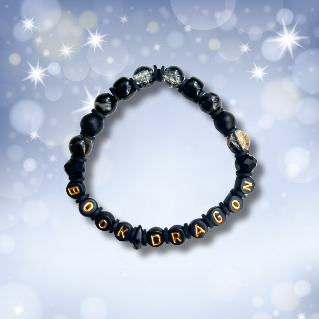 Black beaded bracelet with the words Book Dragon, on a pale blue background with stars.