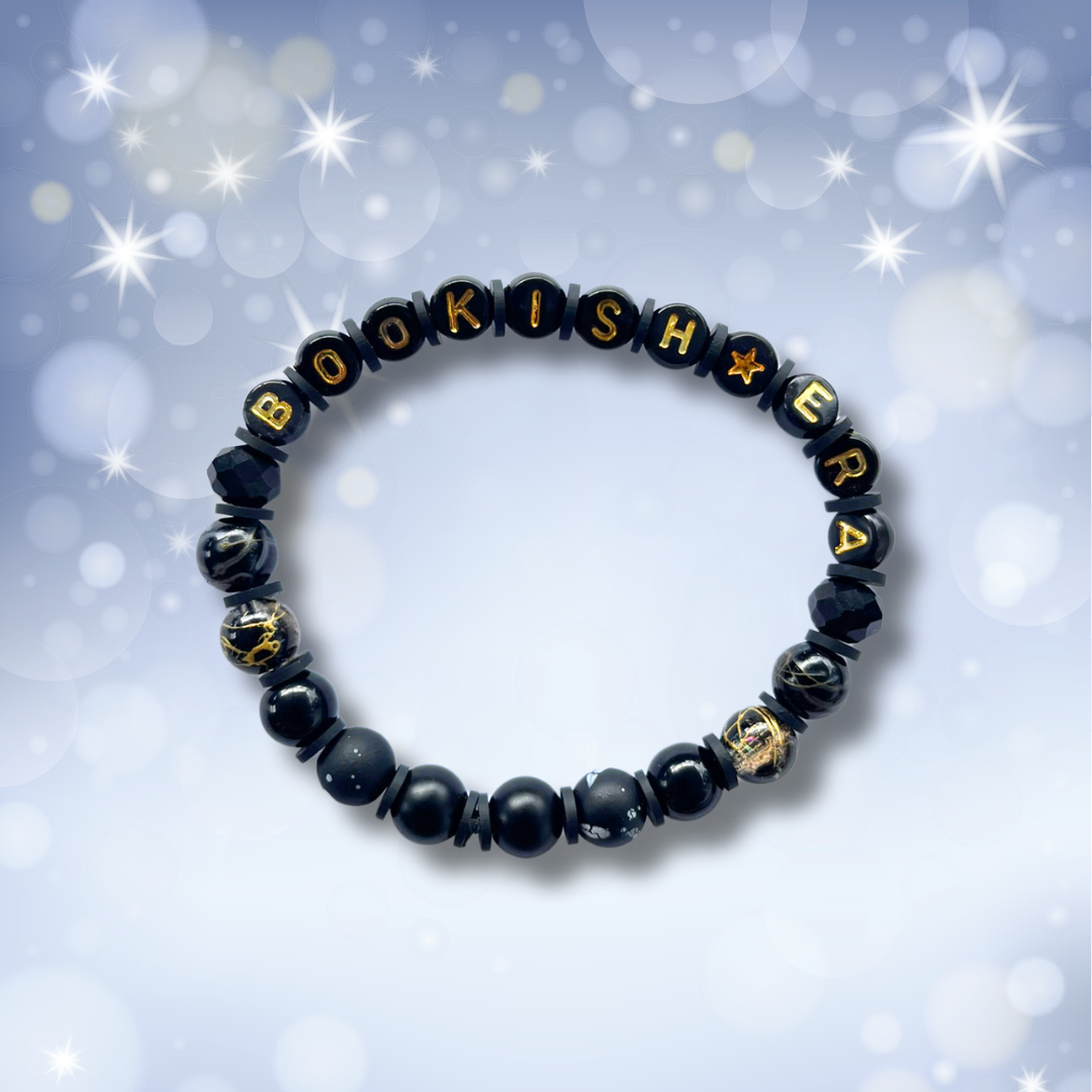 Black beaded bracelet with the words Bookish Era, on a light blue background with stars.