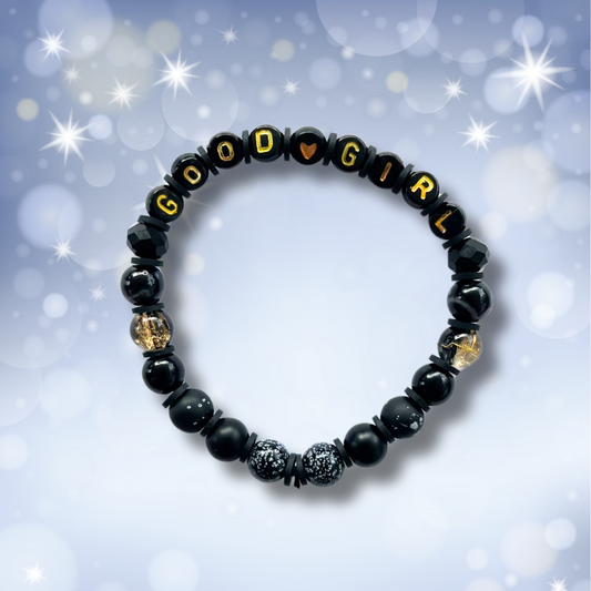 Black beaded bracelet with the words Good Girl, on a light blue background with stars.