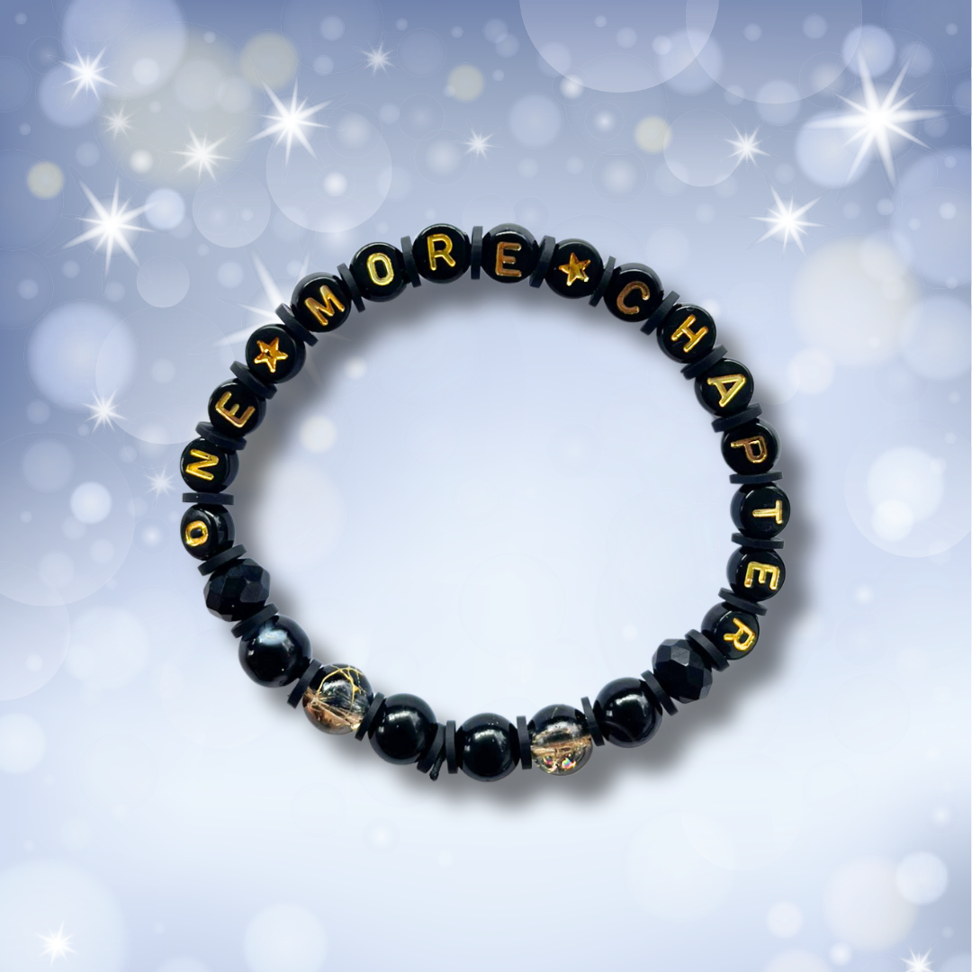 Black beaded bracelet with the words One More Chapter, on a light blue background with stars.