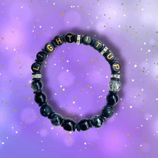 Black beaded bracelet with the words Light It Up, on a purple background with stars.