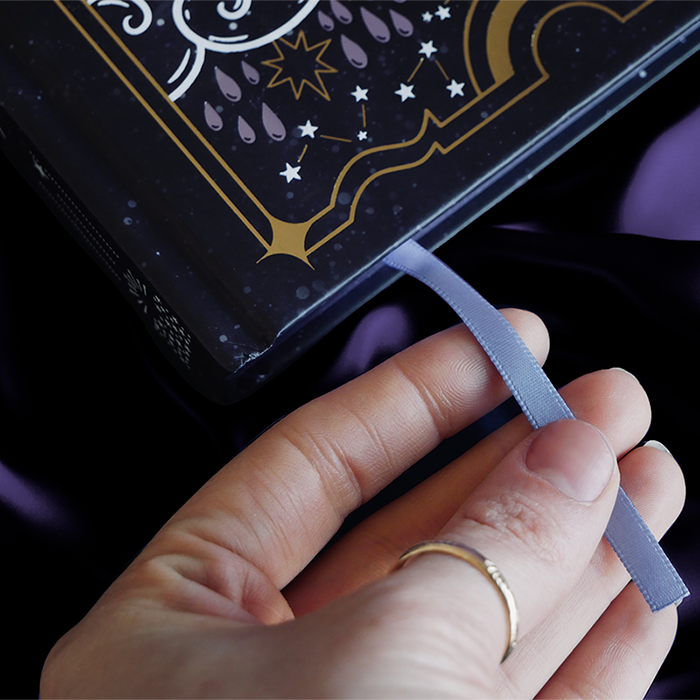 Detail of black journal with intricate gold and purple patterns showing the purple ribbon bookmark.