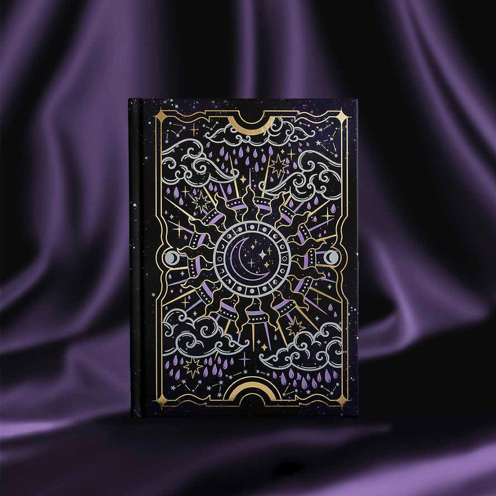 Black journal with intricate gold and purple patterns, shown on a purple satin background.