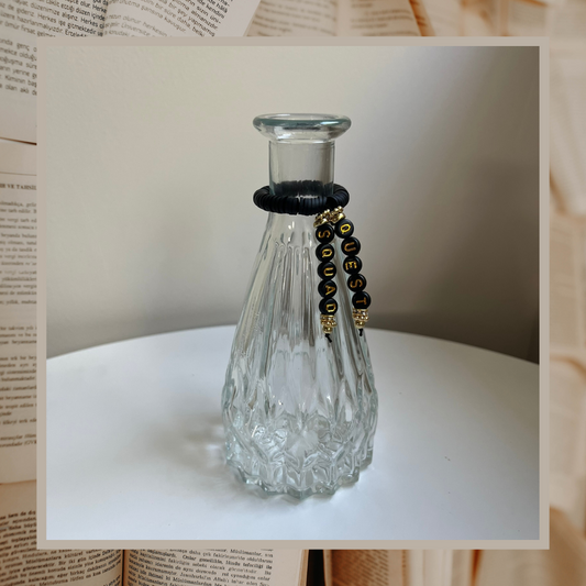 Glass vase with beads that say Quest Squad. Shown on an open books background.