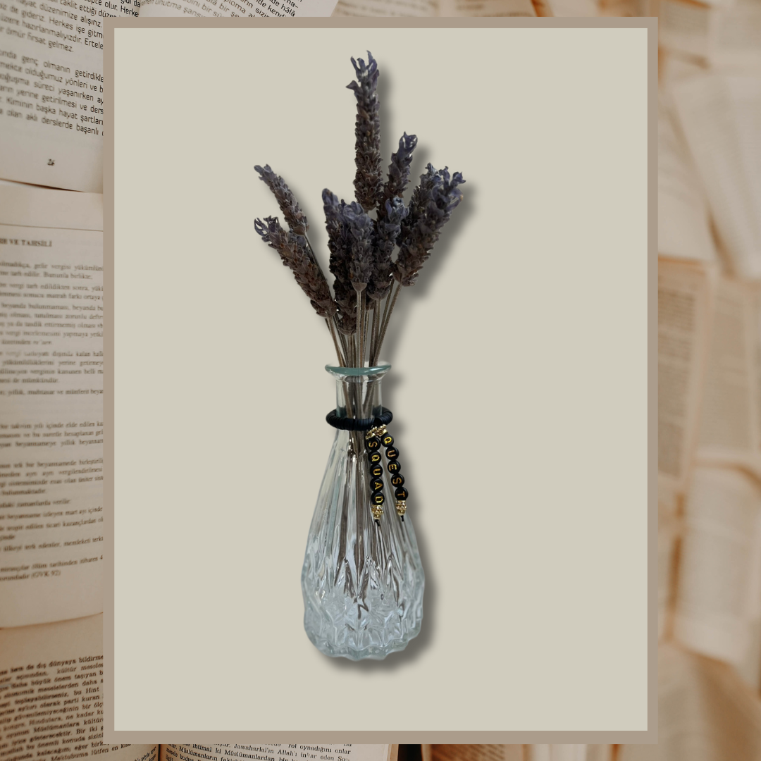 Glass vase with beads that say Quest Squad. Vase with lavender in it, shown on an open books background.