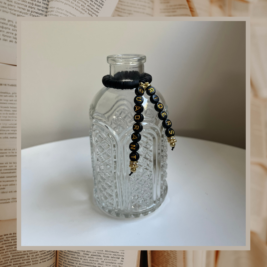 Glass vase with beads that say Riders Quadrant. Shown on an open books background.