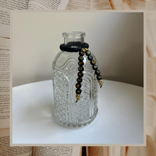 Glass vase with beads that say Riders Quadrant. Shown on an open books background.