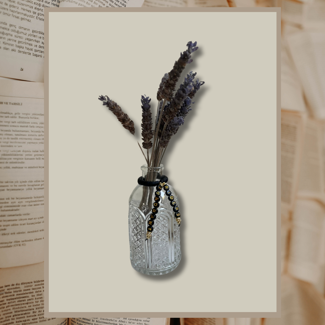 Glass vase with beads that say Riders Quadrant. Vase with lavender in it, shown on an open books background.