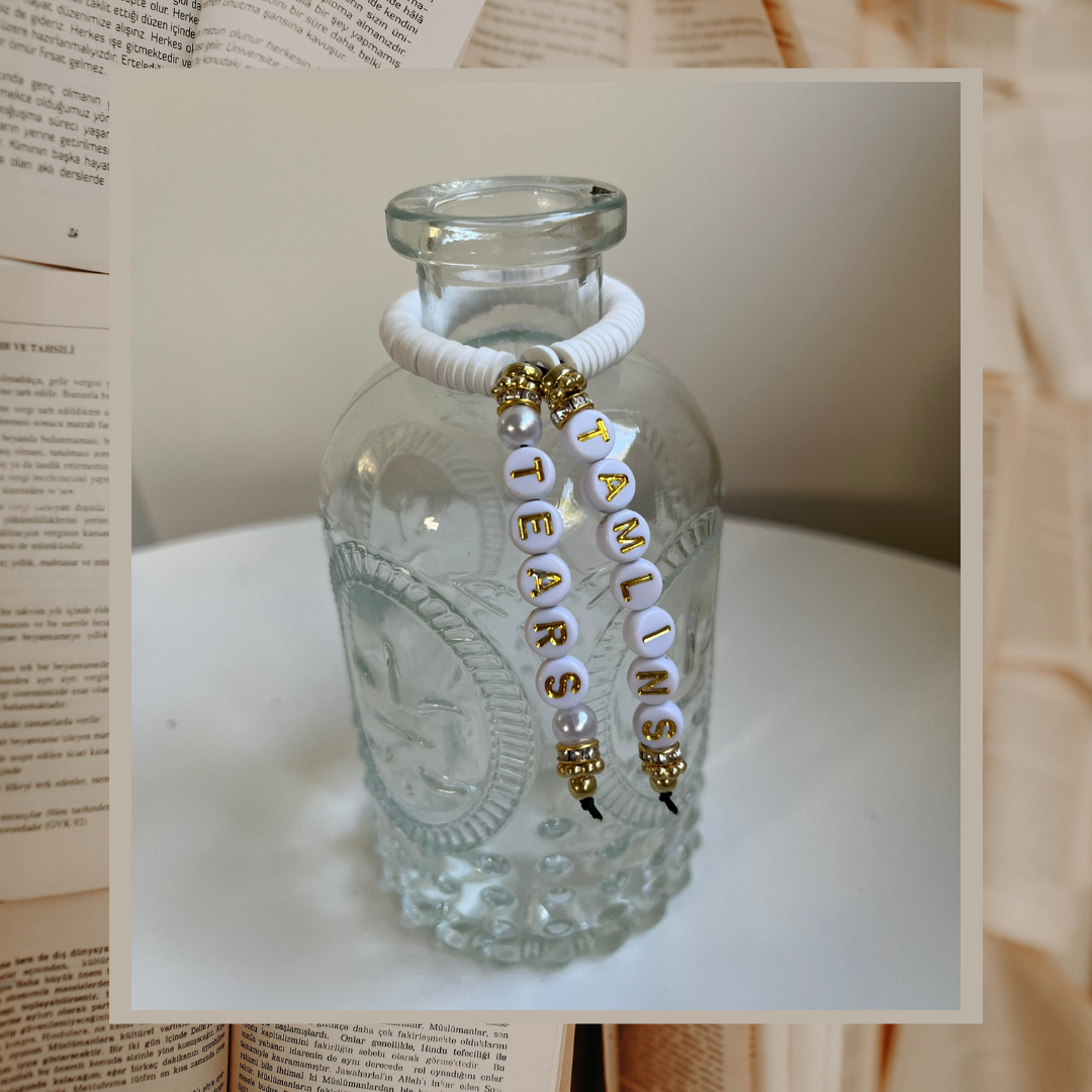 Glass vase with beads that say Tamlins Tears. Shown on an open books background.