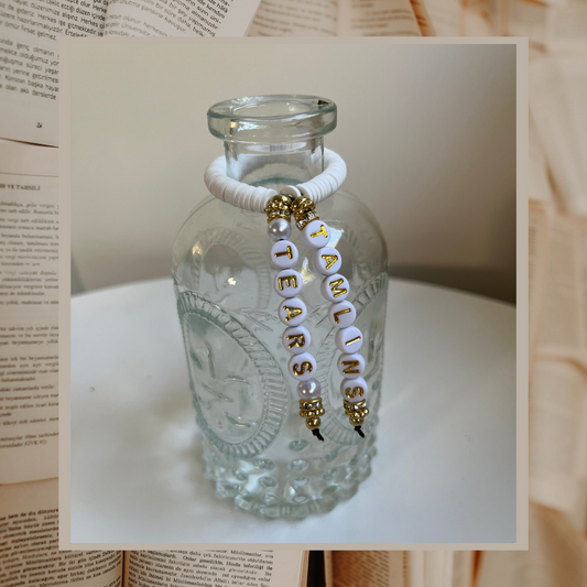 Glass vase with beads that say Tamlins Tears. Shown on an open books background.