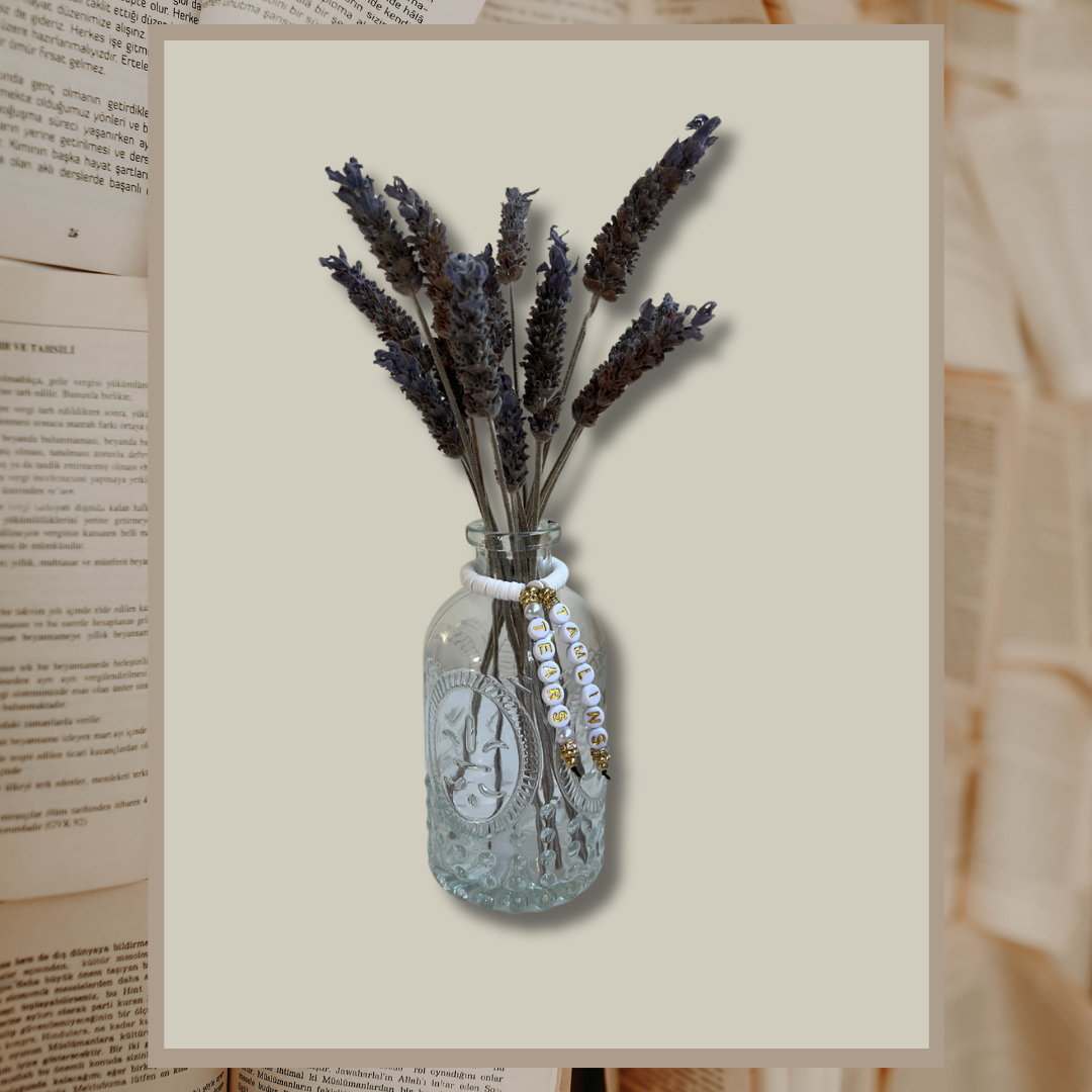 Glass vase with beads that say Tamlins Tears. Vase with lavender in it, shown on an open books background.