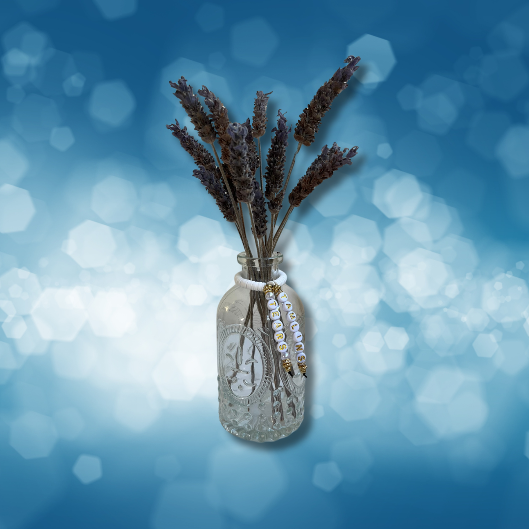 Glass vase with beads that say Tamlins Tears. Vase with lavender in it, shown on a blue background.