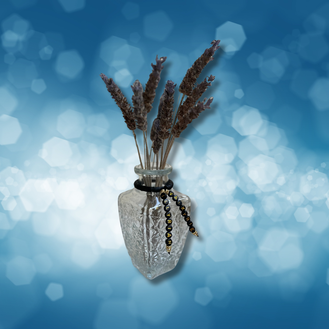 Glass vase with beads that say Valkyrie and Illyrian. Vase with lavender in it, shown on a blue background.