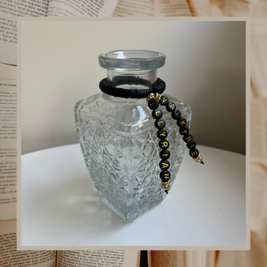 Glass vase with beads that say Valkyrie and Illyrian. Shown on an open books background.