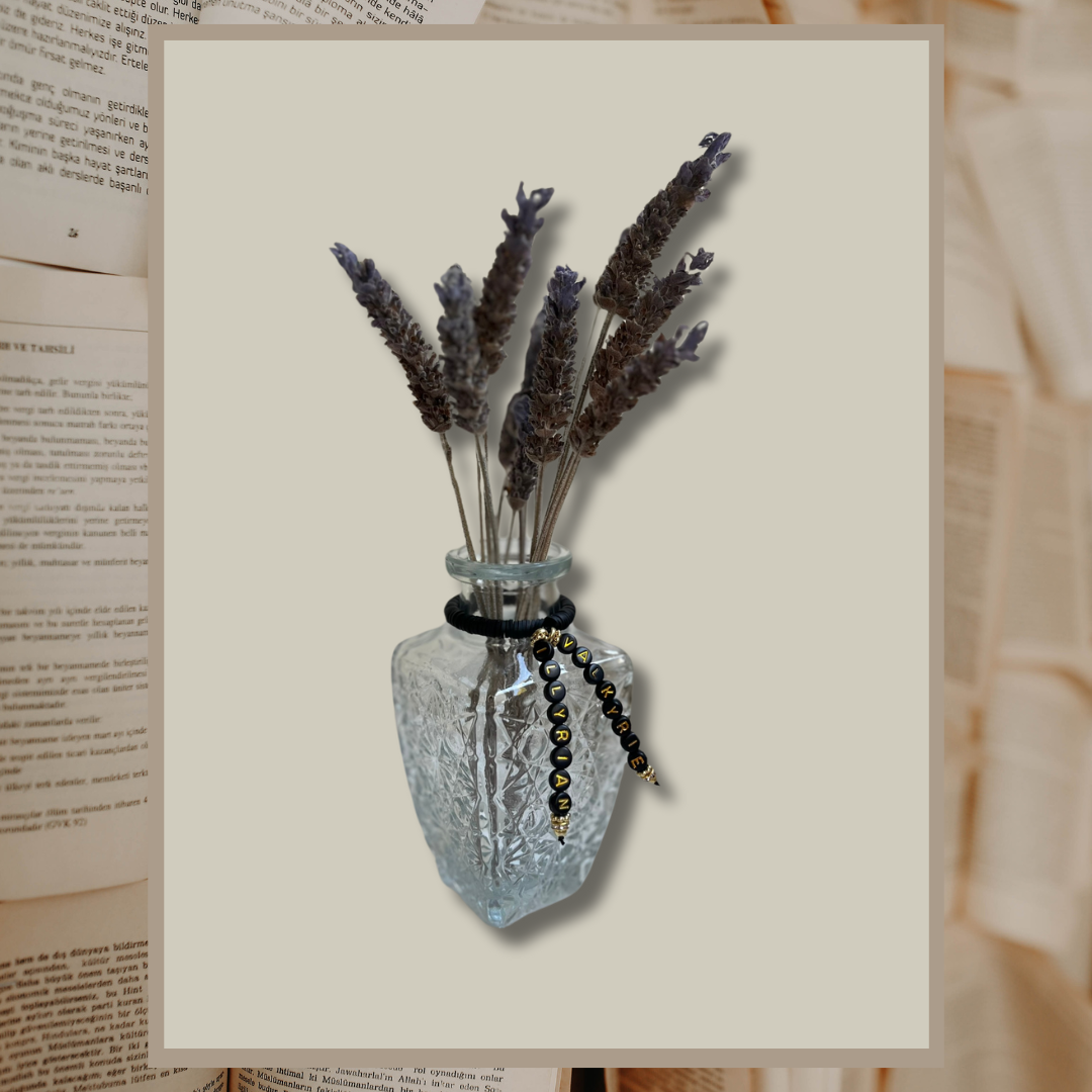 Glass vase with beads that say Valkyrie and Illyrian. Vase with lavender in it, shown on an open books background.