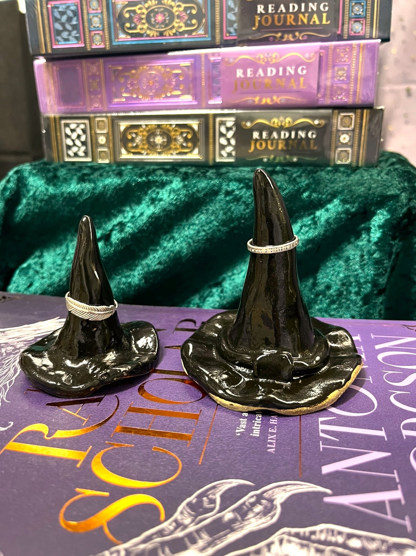 Two black witch hats on a purple book with green velvet background