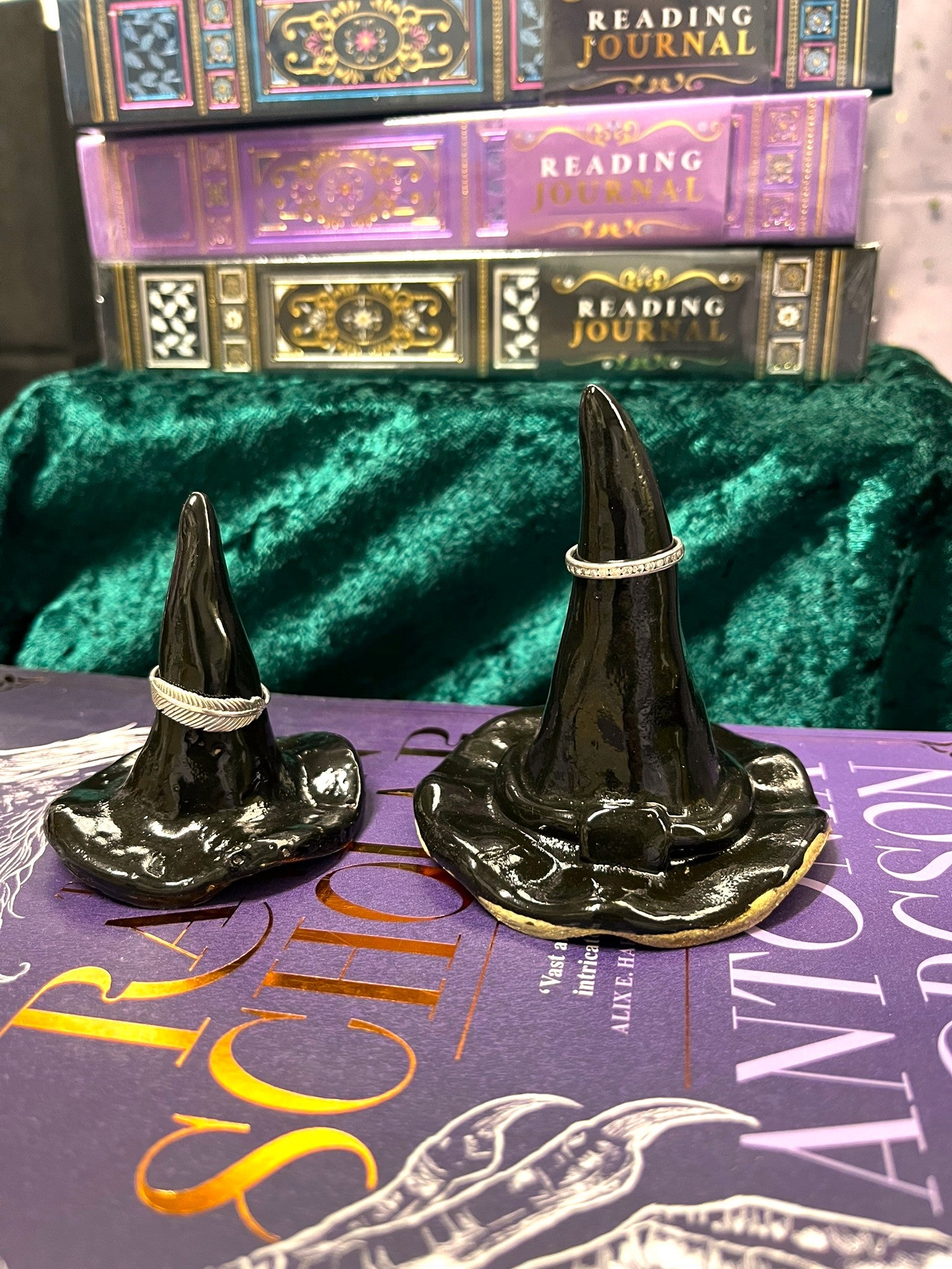 Two black witch hats on a purple book with green velvet background