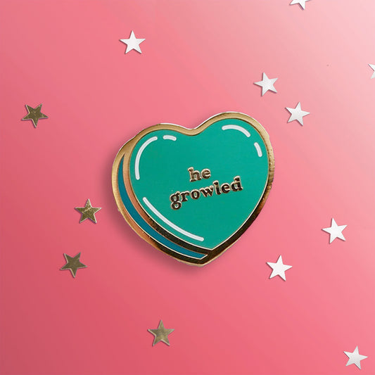 Green heart pin with gold outline: he growled. Shown on a pink background with stars.